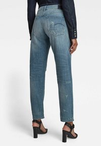 Light blue denim straight-leg jeans with distressed details, featuring back pockets and a high waist, paired with black heeled sandals.