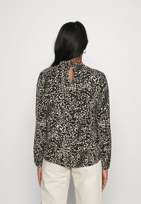 Langærmet bluse i sort og creme med et abstrakt leopardprint, der har høj hals og en nøglehulsåbning bagpå. Blødt stof med rynkede ærmer.