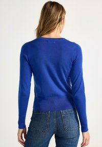 Maglione aderente blu con maniche lunghe e orlo a costine, realizzato in tessuto a maglia liscia. La vista posteriore mostra un design semplice e senza cuciture.