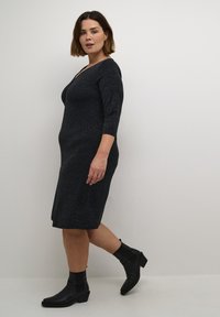 Robe texturée gris foncé avec des manches trois-quarts et un col en V, associée à des bottines noires à talon bas.