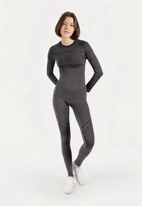 Lichtgewicht zwart sportpak met lange mouwen en nauwsluitende legging. Voorzien van gestructureerde panelen en subtiele branding, geschikt voor actieve kleding.