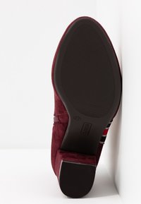 Semelle d'une chaussure en daim bordeaux avec une semelle extérieure en caoutchouc noir texturé et un talon bloc, affichant la pointure 37 et l'étiquette de la marque "Refresh".