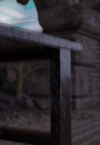 Zapatilla deportiva turquesa con rayas blancas, con parte superior texturizada y suela transparente, colocada sobre una superficie de madera oscura.