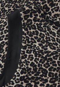 Látka s leopardím vzorem se černým akcentem na okraji. Měkký, strukturovaný materiál v béžových a tmavých odstínech, s různými černými skvrnami.