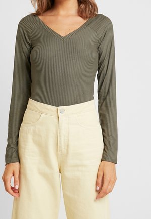 Olivgrüner, gerippter Langarm-Body mit V-Ausschnitt, kombiniert mit hochtaillierten, cremefarbenen Hosen mit weitem Bein und seitlichen Taschen.
