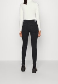 Jeans negros de cintura alta con un corte ajustado, que cuentan con bolsillos traseros, detalles de costura y un parche con el logo en la cintura.