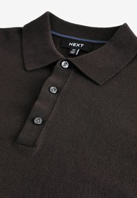 Polo de color marrón oscuro con cuello, tapeta de tres botones y tejido texturizado. La etiqueta de la marca es visible en el interior del cuello.