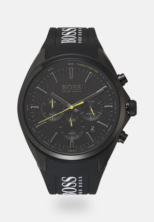 Montre-bracelet noire Hugo Boss avec tachymètre, trois sous-cadrans pour les minutes, les secondes, les 24 heures, et aiguilles jaunes des secondes et des sous-cadrans.