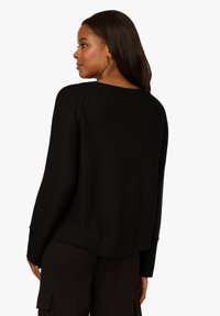 Černý pletený svetr s kulatým výstřihem, ribbovanými manžetami a lemem. Má texturovaný vzor a volný střih, viděný z zadní strany.