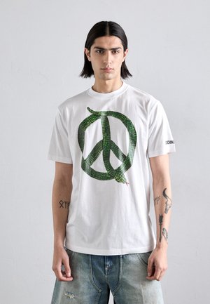Camiseta blanca de algodón con una serpiente verde formando un símbolo de paz en el frontal; mangas cortas, cuello redondo, ajuste casual.
