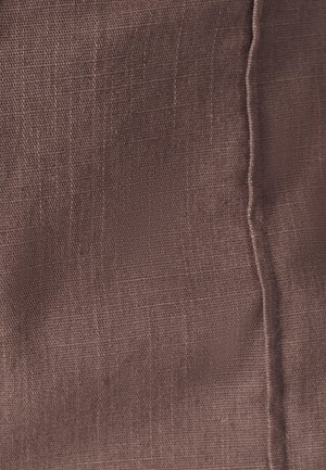 Tekstiili hillityssä ruskeassa sävyssä, jossa on teksturoitu pinta, hienovarainen kudottu kuvio ja näkyvä ompelu reunan varrella.