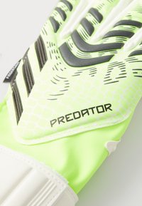 Guanto da portiere verde e bianco con grip testurizzato, motivo a nido d'ape e logo "PREDATOR". Presenta dita imbottite per un maggiore supporto.