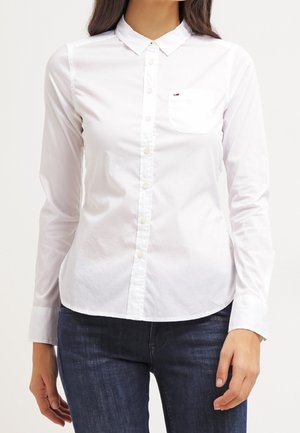Biała koszula na guziki z kołnierzykiem, długimi rękawami, przednią kieszenią oraz subtelnym logo marki. Wykonana z gładkiego, tkanego materiału o klasycznym kroju.