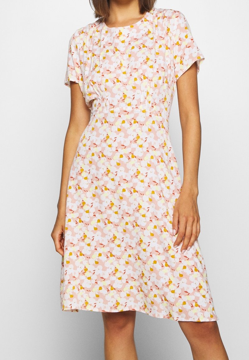 Robe florale rose à manches courtes, avec des motifs de fleurs blanches et jaunes sur un tissu texturé. Silhouette en A avec des détails de fronces subtils.