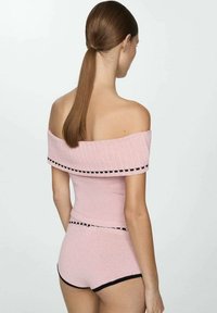 Světlounce růžový pletený top s odhalenými rameny a černým lemováním, doplněný o sladěné šortky s vysokým pasem. Hladká textura, přiléhavý střih.