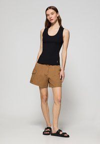 Top in cotone nero a costine, pantaloni cargo marroni con tasche laterali e sandali neri. L'outfit presenta un design casual e materiali leggeri.