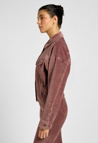 Giacca di velluto a coste rosa con un frontale a bottoni, grandi tasche e taglio rilassato, caratterizzata da una texture a coste e maniche con risvolto.