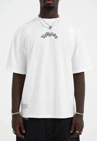 White cotton t-shirt with short sleeves, featuring black "Ed Hardy" logo on the front and additional branding at the bottom left.