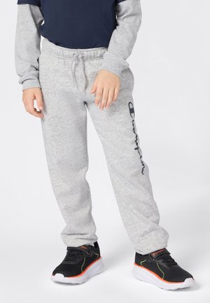 Child wearing light gray Champion sweatpants with a logo on the left leg and black sneakers with white soles and orange detailing.
