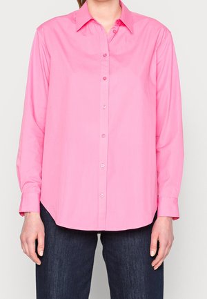 Chemise à manches longues rose pâle avec col, présentant un ourlet droit et un léger brillant, associée à un pantalon en denim foncé.