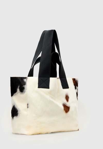 Sac fourre-tout avec motif en cuir de vache noir et marron, avec de larges poignées en tissu noir cousues sur les côtés supérieurs.