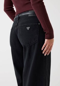 Sorte denim jeans med en afslappet pasform, der har et trekantet logo på baglommen og et læderbælte med prægede detaljer.