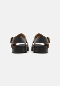 Sandali in pelle nera con dettagli marroni, design open back, suola nera spessa, chiusura con fibbia regolabile e dettagli con cinturino.