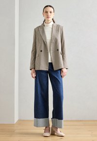 Blazer croisé en vichy beige et marron, associé à un jean bleu à jambes larges avec un ourlet gris et des chaussures tissées beiges.