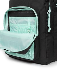 Zaino nero con una tasca frontale verde menta, dotato di zip e dettagli in rete. Tessuto lucido, forma rettangolare e hardware regolabile.