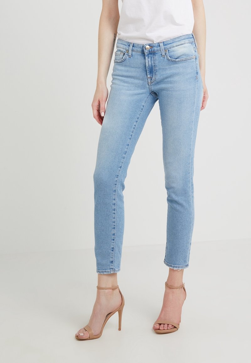 Jeans de denim azul claro con corte ajustado, que cuentan con cinco bolsillos, una cremallera en la bragueta y dobladillo deshilachado. Combinados con sandalias de tacón con tiras en color nude.