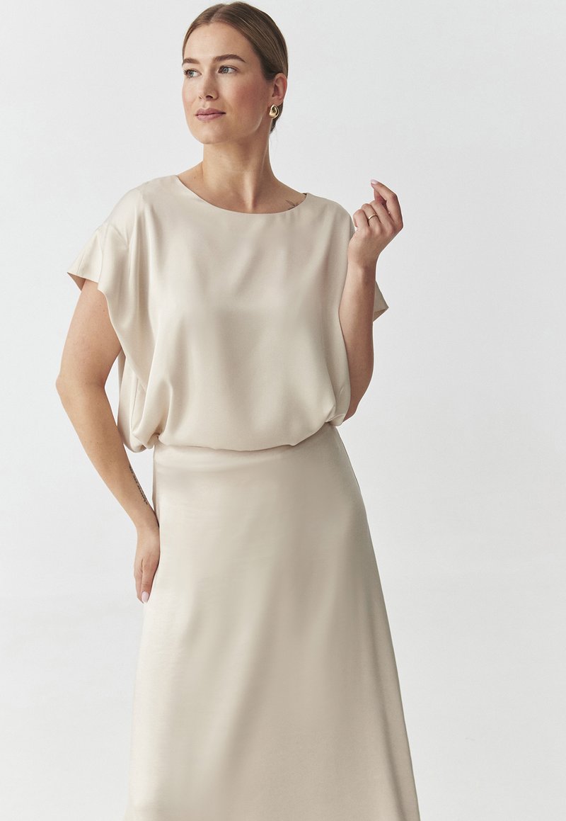 Abito beige in satin con una vestibilità comoda e maniche corte, caratterizzato da un collo rotondo e un flusso continuo fino a un orlo a mezzaluna.