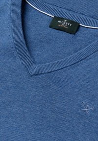 Blauer V-Ausschnitt-Pullover mit einem schwarzen Hackett London Heritage-Label im Kragen und einem kleinen gestickten Logo auf der Brust.