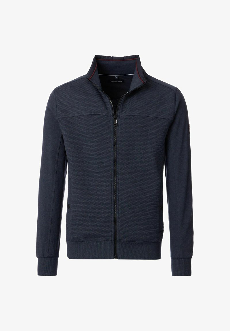Marinekleurige zip-up jack met hoge kraag, gestructureerde stof en rode accenten langs de kraag. Beschikt over ribgebreide manchetten en onderkant.