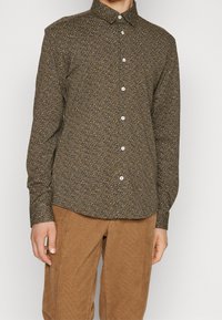 Camicia marrone a bottoni con un motivo testurizzato e piccoli accenti blu, gialli e bianchi. Con colletto, taglio regolare e maniche lunghe.