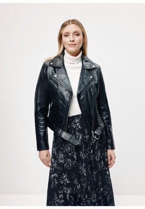 Czarna skórzana kurtka motocyklowa o dopasowanym kroju, z asymetrycznym zapięciem na zamek z przodu i paskiem w talii, zestawiona z białym golfem i kwiecistą spódnicą.