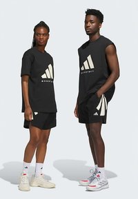 Crna sportska odjeća s bijelim detaljima. Žena nosi majicu labavog kroja i kratke hlače; muškarac nosi top bez rukava i kratke hlače. Oboje imaju tenisice.