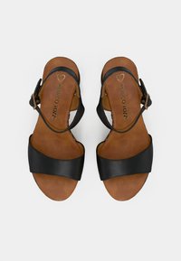 Μαύρα δερμάτινα σανδάλια με καφέ σόλα, διαθέτοντας φαρδύ μπροστινό λουρί και ρυθμιζόμενο λουρί στον αστράγαλο με αγκράφα. Το όνομα της μάρκας είναι εγχάραξο στο εσωτερικό.