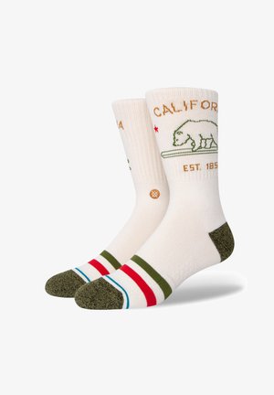 Meias até ao joelho com uma base creme, gráfico de um urso verde, texto "CALIFORNIA" e riscas coloridas em vermelho, verde e azul na ponta e na bainha.