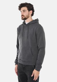 Felpa grigia con cappuccio realizzata in tessuto morbido, dotata di tasca frontale a marsupio, lacci e polsini e orlo a coste. Modello che indossa jeans.