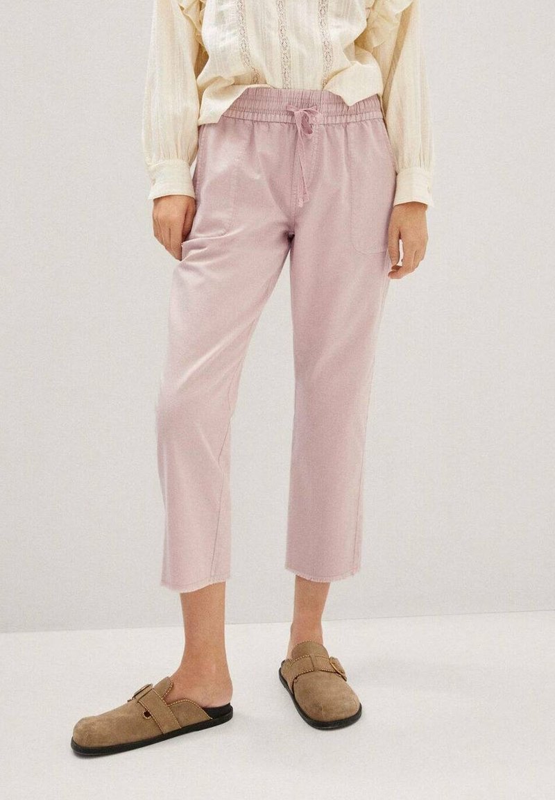 Pantalones cortos de color rosa claro con cintura elástica y cordón, que cuentan con un único bolsillo lateral y dobladillos sin terminar, combinados con zuecos marrones.