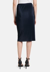 Navy-gestreifter Midirock mit einer figurbetonten Silhouette, elastischem Bund und glattem, glänzendem Material. Kombiniert mit schwarzen, hochhackigen Schuhen mit Knöchelriemen.