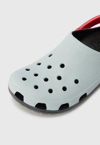 Svetlomodré živicové dreváky s veľkými ventilačnými otvormi, čiernymi podrážkami a červeným popruhom. Textúrovaný povrch s hladkým dokončením.
