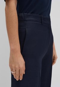 Navyblauwe op maat gemaakte broek met een gladde textuur, enkele plooien en een rechte voorkant. Heeft een tailleband met een lus voor een riem en een subtiele glans.