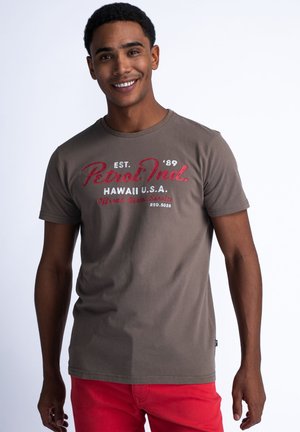 Camiseta de algodón marrón con mangas cortas, que presenta texto impreso en rojo y blanco que dice "Petrol Ind. HAWAI U.S.A." en la parte frontal.