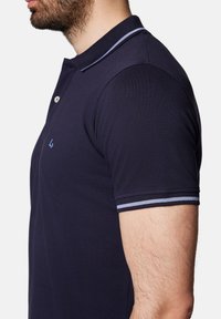 Granatowa koszulka polo z teksturowanej tkaniny, z rozpięciem na dwa guziki oraz kontrastującymi jasnoniebieskimi paskami na kołnierzyku i mankietach.