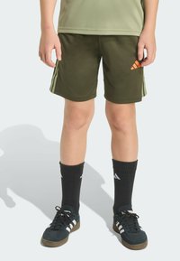 Olive green athletic shorts with three white stripes on the sides, paired with black knee-high socks and dark sneakers with white accents.