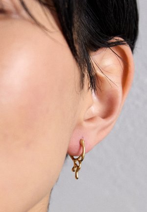 Brinco de argola dourado com um design orgânico e fluido, apresentando acentos texturizados e um acabamento suave, usado num ouvido perfurado.