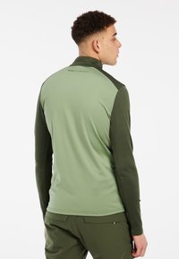 Lichtgroene lange mouwen top met een ritssluiting bij de kraag en donkergroene mouwen, met een gladde textuur en een logo detail op de rug.