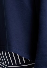 Sudadera azul marino con una textura suave, de corte holgado. Combinada con leggings a rayas negras y blancas en el dobladillo inferior.