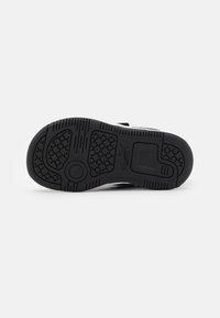 Semelle en caoutchouc noir texturé avec un motif en nid d'abeille. Dispose d'un design élégant et simple avec un logo sur le côté et une zone de talon renforcée.